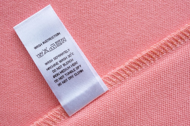 Weiße Wäschepflege Waschanleitung Kleideretikett auf rosa Baumwollhemd