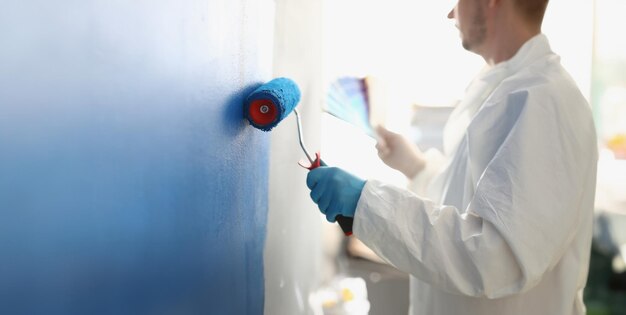 Weiße Wand mit blauer Walze streichen. Dienstleistungen eines Malermeisters für Hausreparaturen