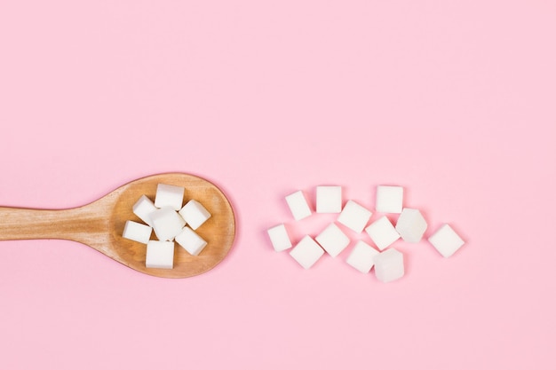 Weiße Zuckerwürfel auf einem Holzlöffel und auf einem rosa Hintergrund in einer Draufsicht