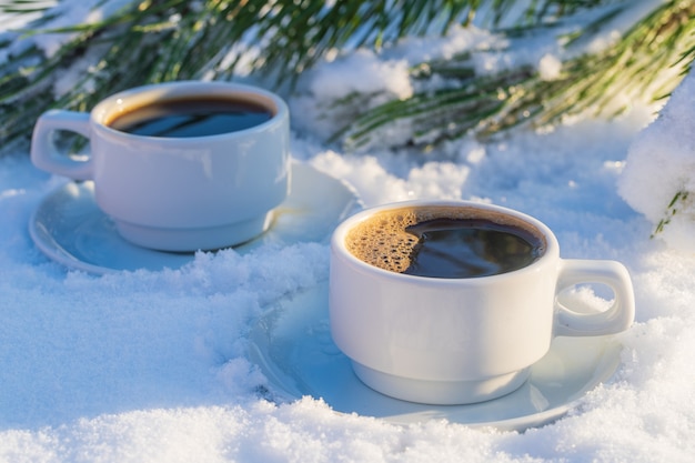 Weiße zwei Tasse heißen Kaffees auf einem Bett aus Schnee und weißem Hintergrund, nah oben. Konzept des Weihnachtswintermorgens