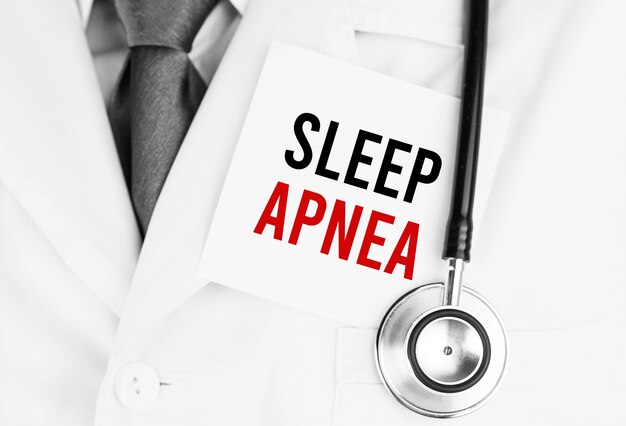 Weißer Aufkleber mit Text SLEEP APNEA, der auf medizinischem Gewand mit einem Stethoskop liegt