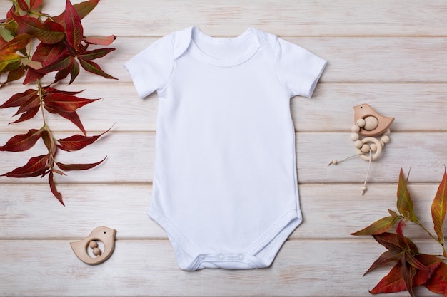 Weißer Baumwoll-Baby-Kurzarm-Strampler mit rotem Fallgras und Vogelspielzeug auf dem hölzernen Hintergrund Design geschlechtsneutrale Bodysuit-Vorlage neugeborener Strampler-Print-Präsentationsmock-up