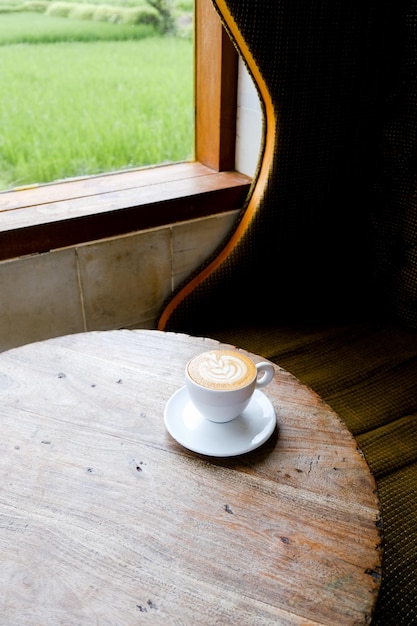 weißer Becher Cappuccino auf hölzernem Hintergrund mit schöner Latte-Kunst