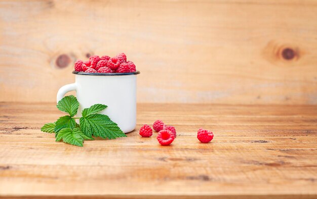 weißer becher mit himbeeren auf hölzernem hintergrund mit kopienraum