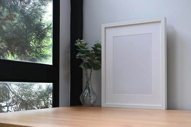 Weißer Bilderrahmen und Topfpflanze auf Holztisch in der Nähe des Fensters