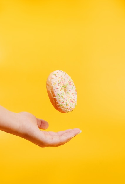 weißer Donut auf einem gelben Hintergrund, der in der Luft über Hand hängt