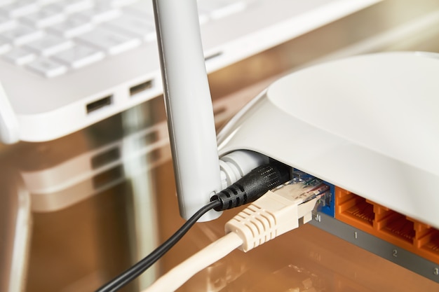 Weißer drahtloser Wi-Fi-Router nahe einem Laptop auf einem Glastisch