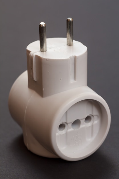 Weißer elektrischer T-Stecker aus Kunststoff mit drei Steckdosen auf schwarzem Hintergrund.