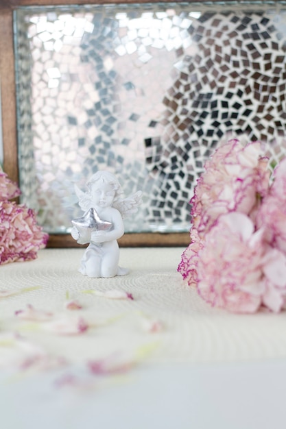 Weißer Engel auf dem Schreibtisch. Schöne rosa Blumen auf weißem Schreibtisch.
