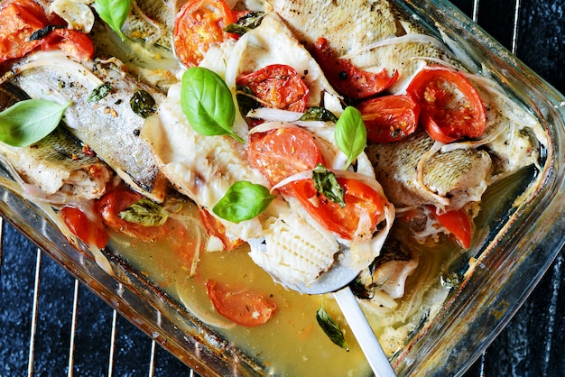 Weißer Fisch (Pollock, Kabeljau, Seehecht), gebacken mit Tomaten, italienischen Kräutern und frischen Basilikumblättern im Basilikum in ihrem eigenen Saft. Leckeres Abendessen mit mediterranen Meeresfrüchten.