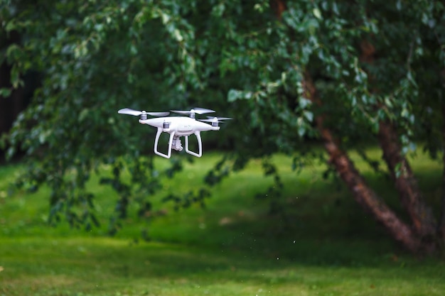 Weißer fliegender Quadrocopter mit Kamera auf grünem Waldhintergrund