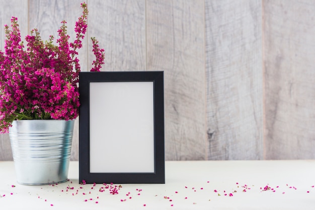 Weißer Fotorahmen und rosa Blumen in einem Aluminiumtopf auf Schreibtisch