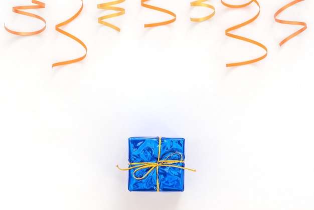 Weißer Hintergrund der Feier mit blauer Geschenkbox mit Goldband, helle Party-Luftschlangen.