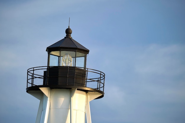 Weißer hoher Leuchtturm am Meeresufer gegen den blauen Himmel für die Navigation von Handelsschiffen