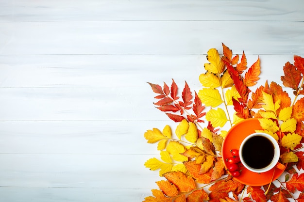 Weißer Holztisch verziert mit Herbstlaub und einem Tasse Kaffee. Herbsthintergrund mit Exemplarplatz.