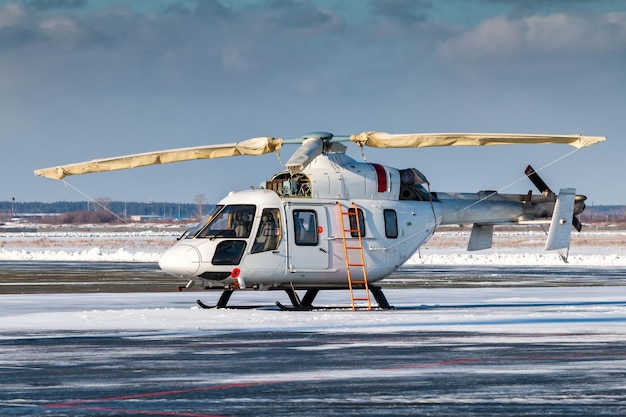 Weißer Hubschrauber mit offenem Motor auf dem Vorfeld eines Winterflughafens