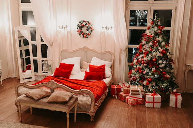 Weißer Innenraum des klassischen Schlafzimmers des neuen Jahres mit verziertem Weihnachtsbaum in den klassischen weißen und roten Farben mit anwesenden Geschenkboxen.