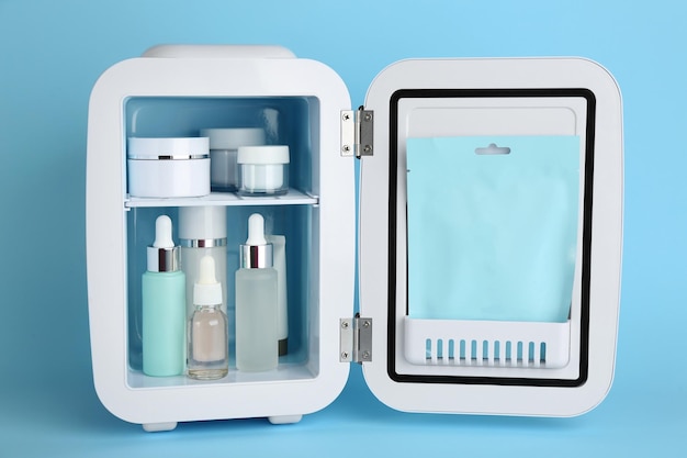 Weißer Kosmetikkühlschrank mit Hautpflegeprodukten auf hellblauem Hintergrund