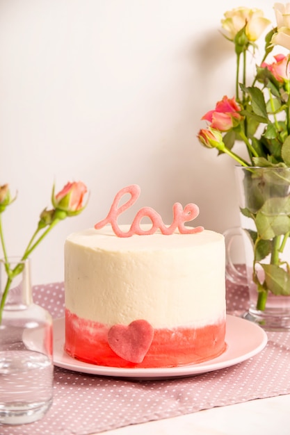 Weißer Kuchen mit rosa Dekor und die Wortliebe auf die Oberseite unter kleinen weißen und rosa Rosen