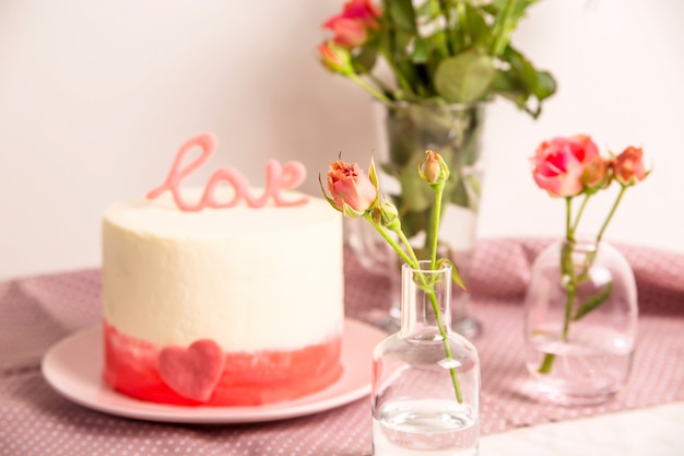 Weißer Kuchen mit rosa Dekor und die Wortliebe auf die Oberseite unter kleinen weißen und rosa Rosen