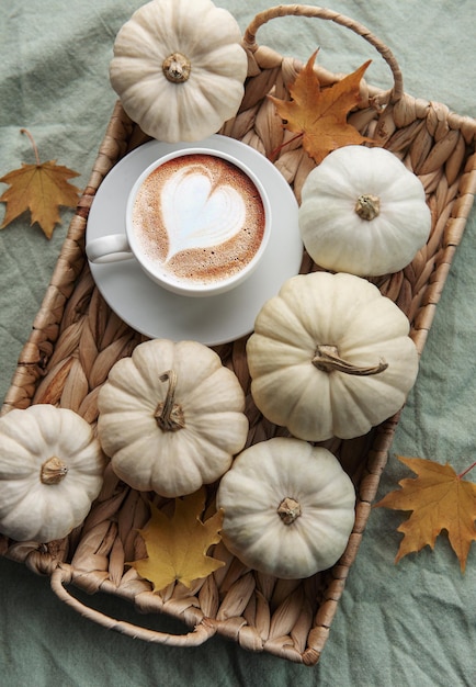 Weißer Kürbiskaffee und Herbstlaub auf einem Weidentablett