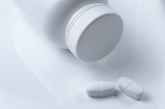 Weißer Kunststoff-Medizinglas und zwei weiße Pillen heller Hintergrund
