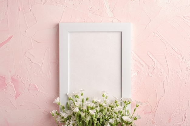 Weißer leerer Fotorahmen mit Mausohr-Vogelmiereblumen auf rosa strukturiertem Tisch, Kopierraum der Draufsicht