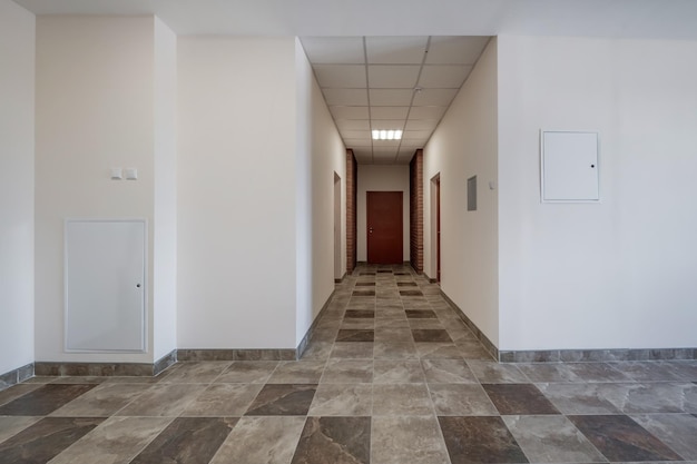 Weißer, leerer, langer Korridor mit roten Backsteinwänden im Inneren moderner Apartments, Büros oder Kliniken