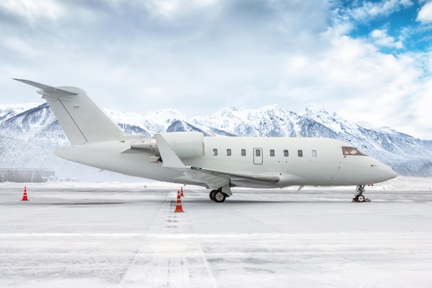 Weißer Luxus-Business-Jet auf dem Vorfeld des Winterflughafens vor dem Hintergrund hoher malerischer Berge