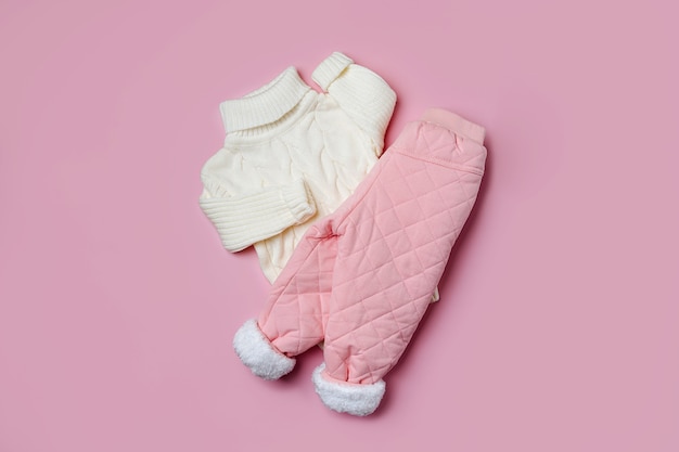 Weißer Pullover und warme Hosen auf rosa Hintergrund. Stylische Kinderoberbekleidung. Wintermode-Outfit