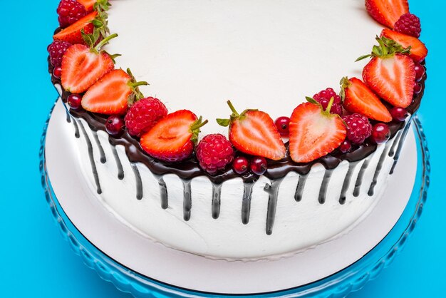 Weißer Quarkkuchen mit Beeren und Himbeeren dekoriert und mit Schokolade beträufelt auf blauem Hintergrund Süßspeisen hausgemachtes Gebäck