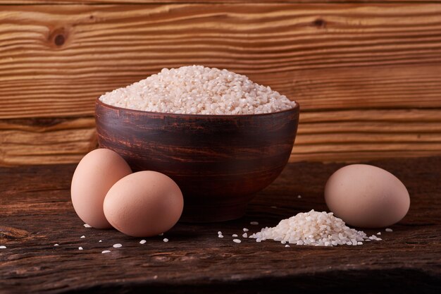 Weißer Reis in der Lehmschüssel auf Tabelle und Eiern auf hölzernem Hintergrund