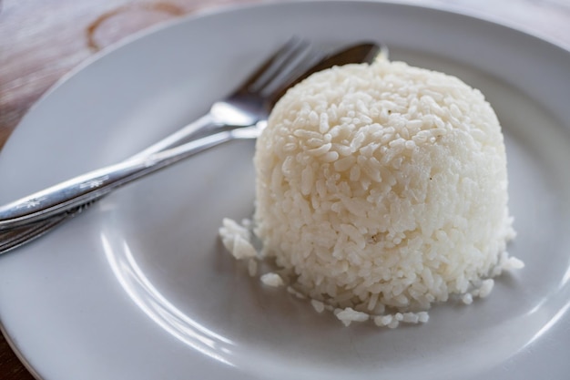 Weißer Reis mit Löffel und Gabel auf weißem Teller
