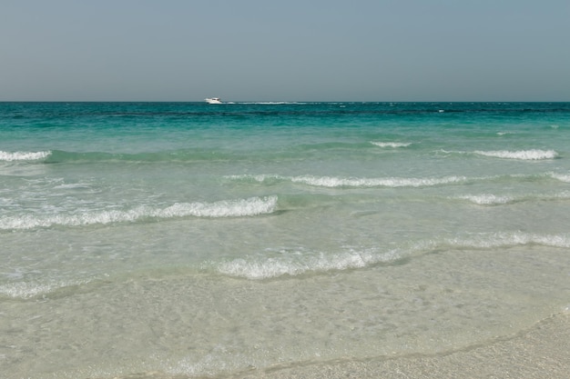 Weißer Sandstrand, blaues, klares Meer, Yacht, Wasserwellen, klarer Himmel