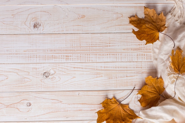 Weißer schal und trockenes gelb verlässt auf einem holztisch. herbst hintergrund, exemplar.