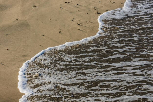 Weißer Schaum im Wasser aus dem Meer mit Sandstrand