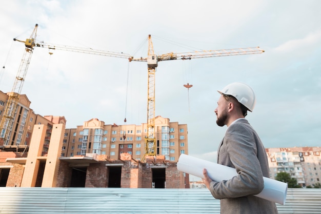 Foto weißer schutzhelm der männlichen ingenieurabnutzung und halten des planes auf baustelle