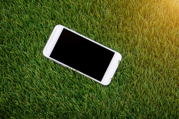 Weißer Smartphone mit lokalisiertem Schirm auf gefälschtem Gras