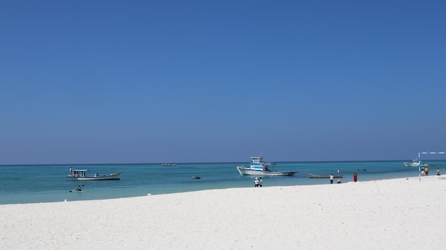 Weißer Strand über dem blauen Ozean mit Segelbooten unter dem blauen Himmel auf der Insel Lakshadweep, Indien