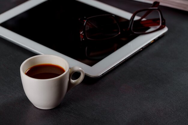 Weißer Tablet-Computer auf einem Holztisch mit Gläsern, eine Schale schwarzer Kaffee