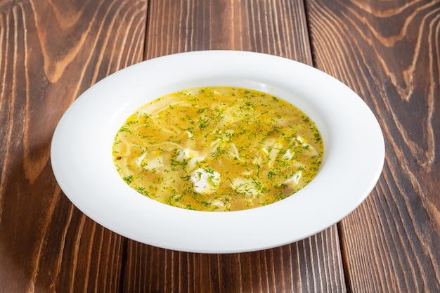 Foto weißer teller der heißen hühnersuppe mit nudeln auf holztisch