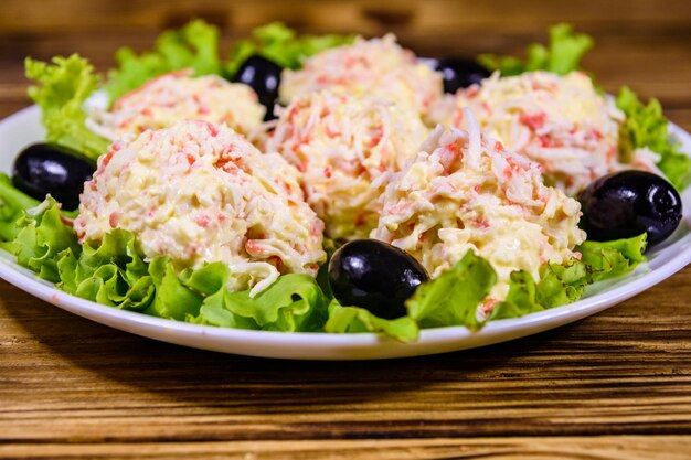 Foto weißer teller mit crabcheese-bällchen, schwarzen oliven und salatblättern auf rustikalem holztisch