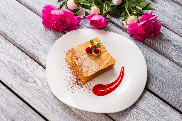 Weißer Teller mit Dessert. Rosa Blumen und rote Beeren. Französisches Rezept für Sommerdessert. Himbeer Millefeuille mit Minze.