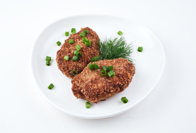 Weißer Teller mit gebratenen Schnitzeln und Kräutern auf Weiß