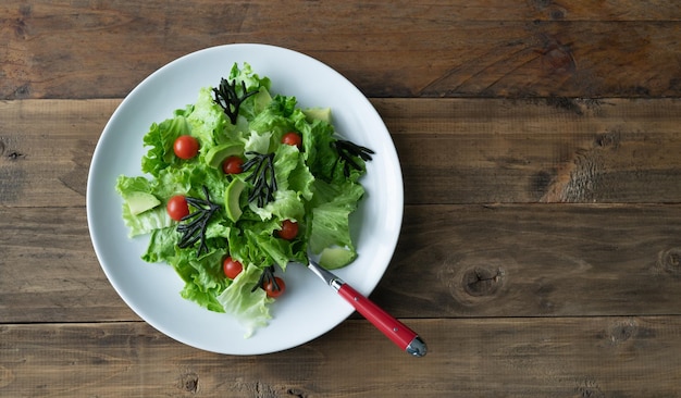 Weißer Teller mit gemischtem Salat mit Algen, Tomaten, Salat und Avocado Holzhintergrund Kopierbereich