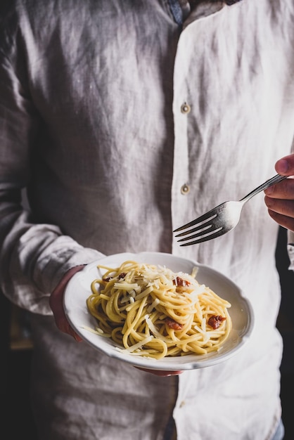 Weißer Teller mit klassischen Carbonara-Nudeln in männlichen Händen