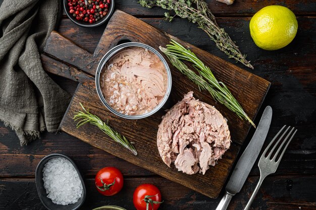 Foto weißer thunfisch in dosen auf holzschneidebrett auf altem dunklem holztischhintergrund xa mit kräutern und zutaten draufsicht flach gelegt