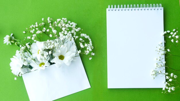 Weißer Umschlag mit Blumen und ein offenes Notizbuch mit einem leeren Blatt Papier