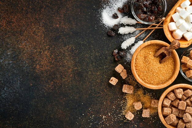 Weißer Zucker, Rohrzuckerwürfel, Karamell in Bambusschale auf dunkelbraunem Tischbeton