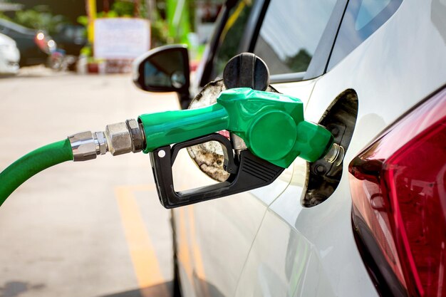 Weißes Auto tanken an Tankstelle mit grüner Zapfpistole.